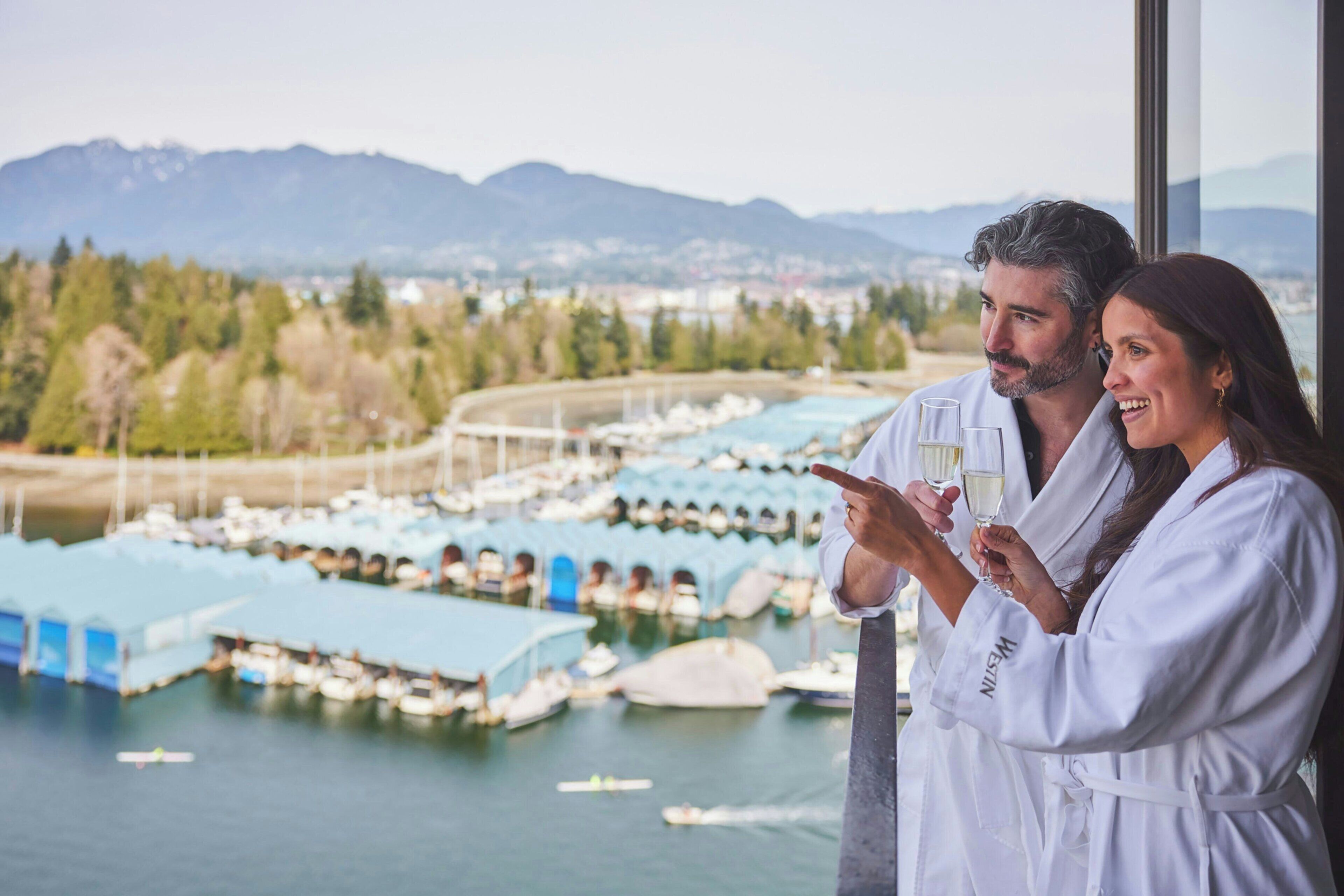 A couple in white robes overlooking a marina with boats and mountains in the background.