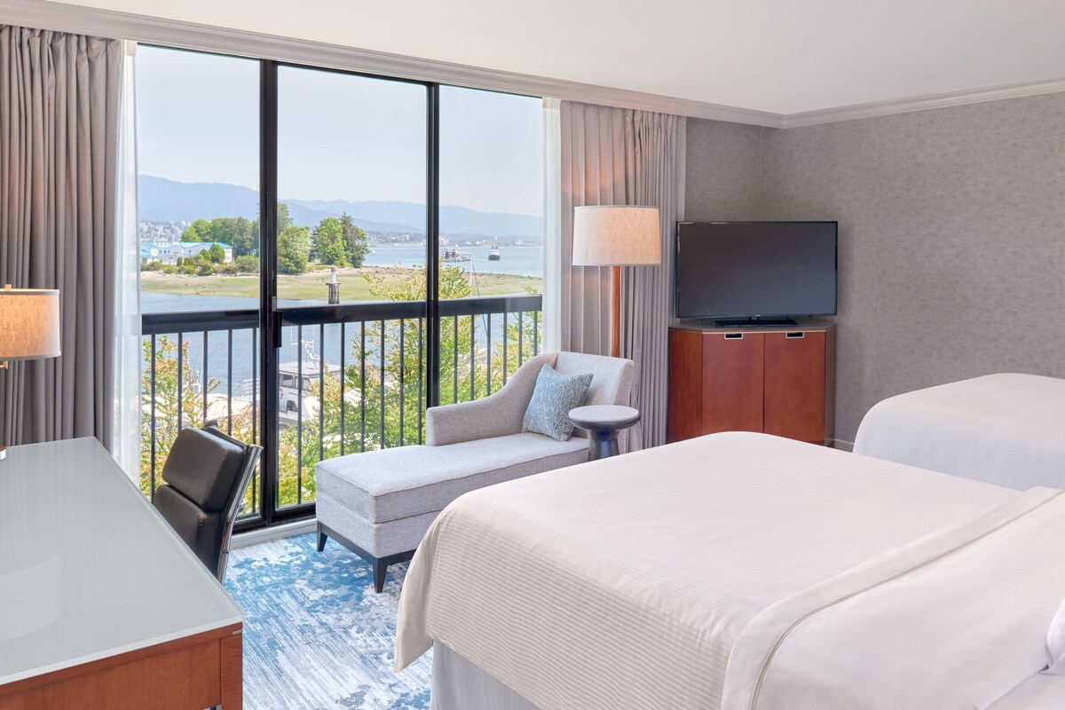 A hotel room with a large balcony, a TV, a sofa, and two beds.