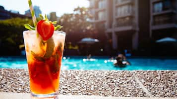 Un vaso de bebida helada adornado con fresa y menta, sobre una superficie pedregosa cerca de una piscina con un edificio al fondo.
