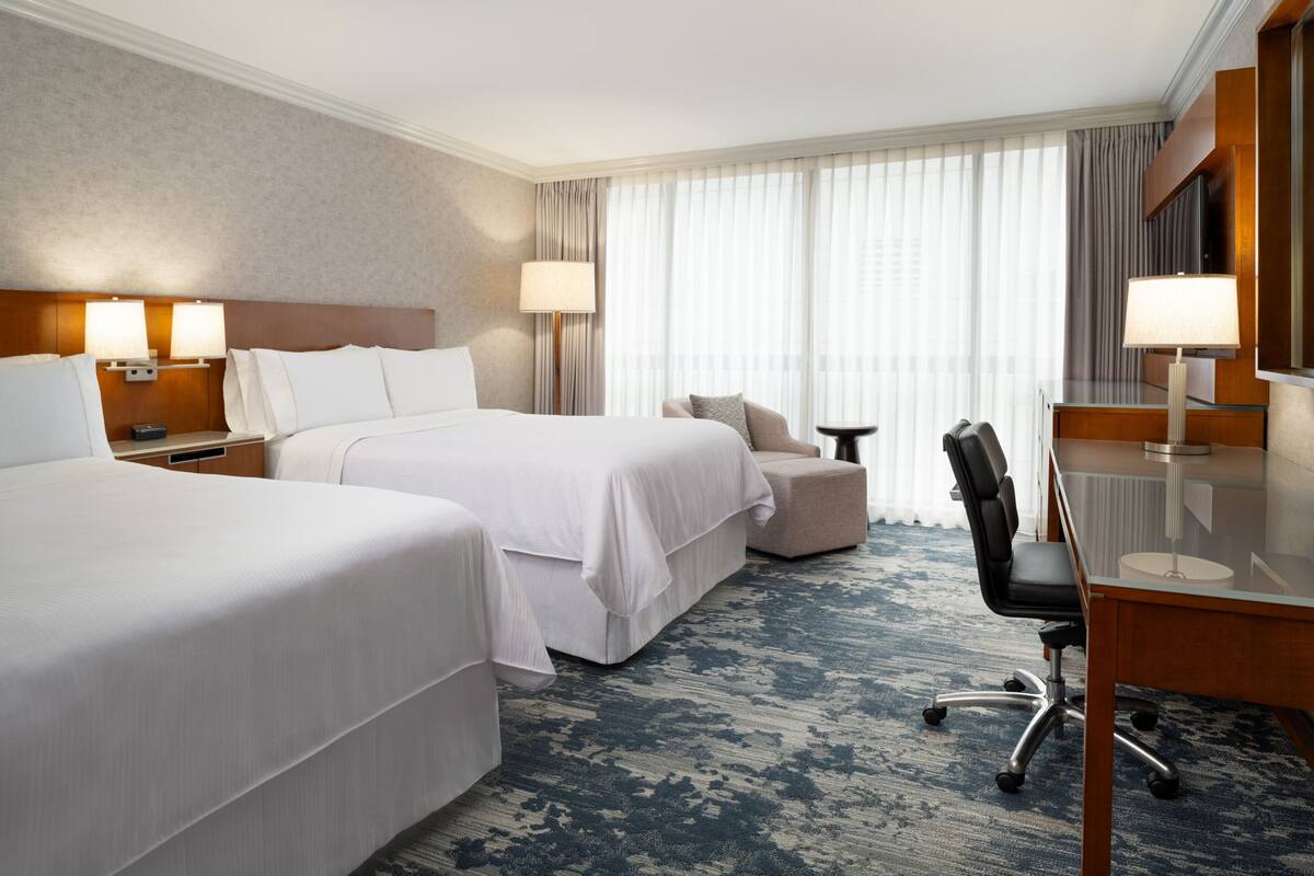 A hotel room with two beds, a desk, a chair, and a small table.