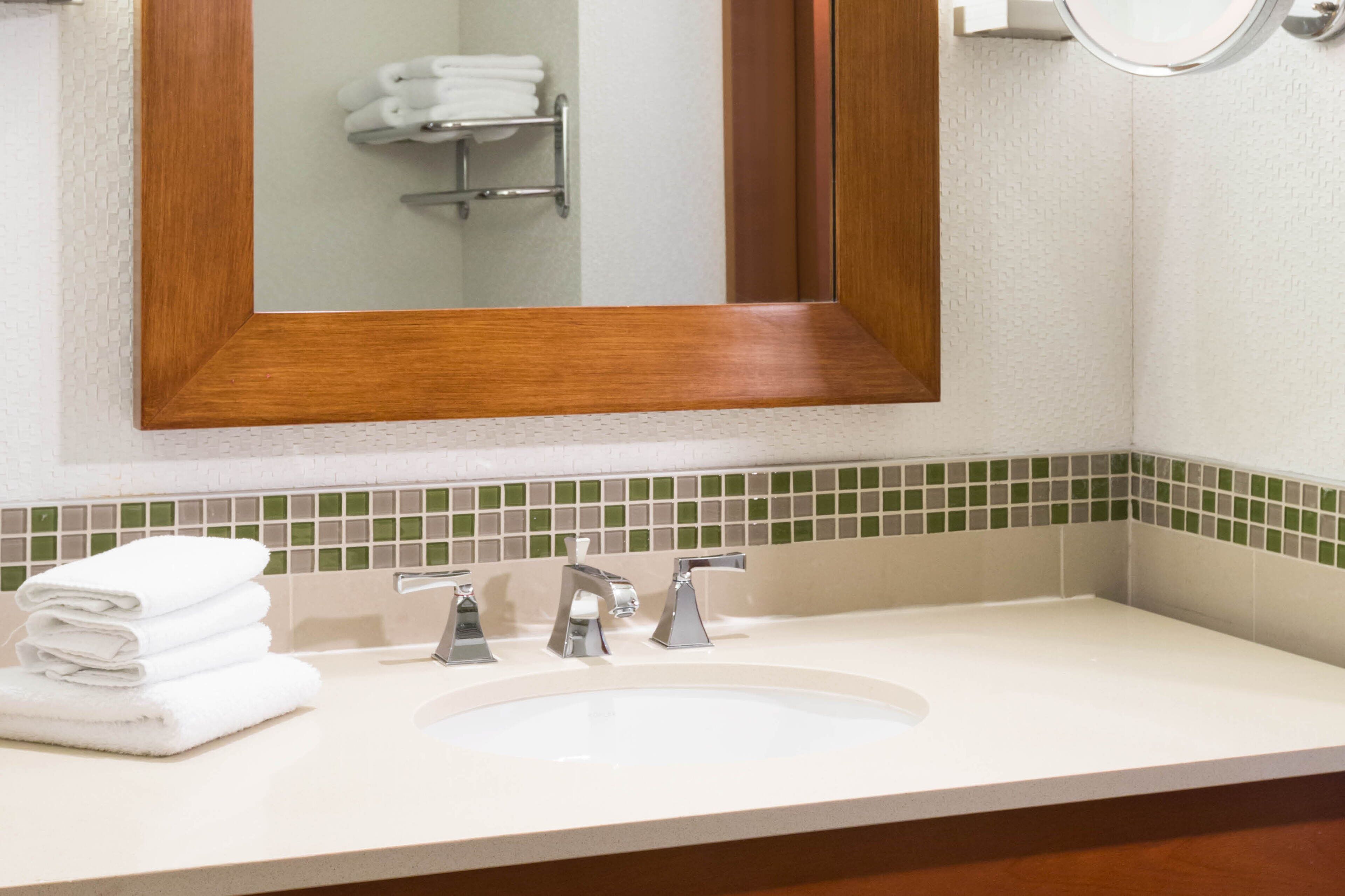 A bathroom with a white sink, two faucets, and a mirror with a wooden frame.