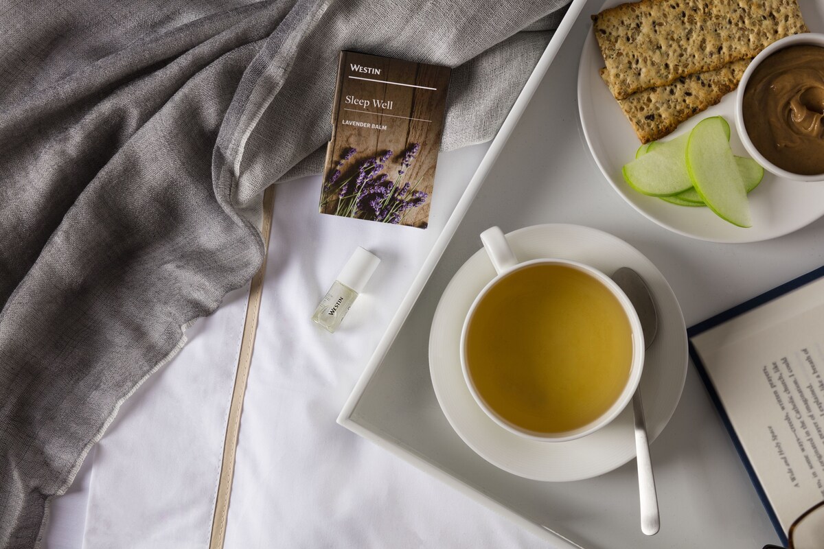 A tray with a cup of tea, a book titled 'Sleep Well Lavender Balm', crackers, apple slices, and a bottle of lotion.