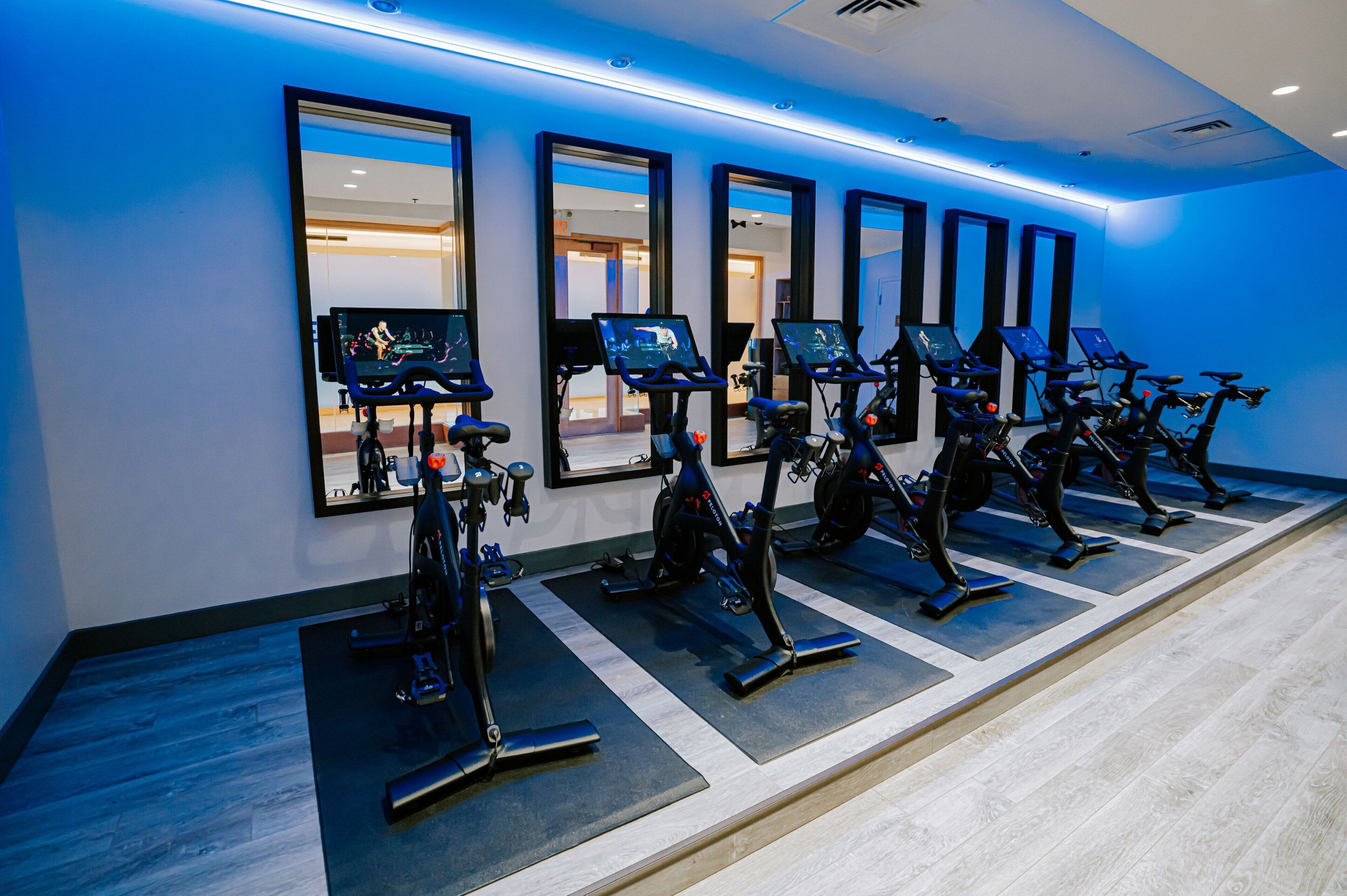 Une rangée de vélos d’appartement dans une salle de sport, avec des miroirs sur le mur.