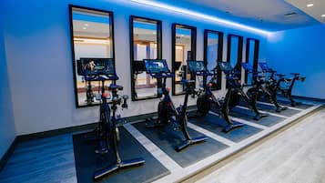 A row of stationary bikes in a gym with mirrors on the wall.