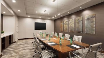A conference room with a long table, chairs, a flat-screen TV, and abstract art on the wall.