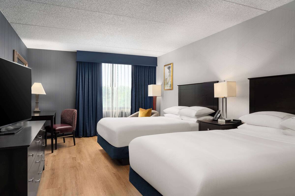 A hotel room with two beds, a desk, a chair, and a television.