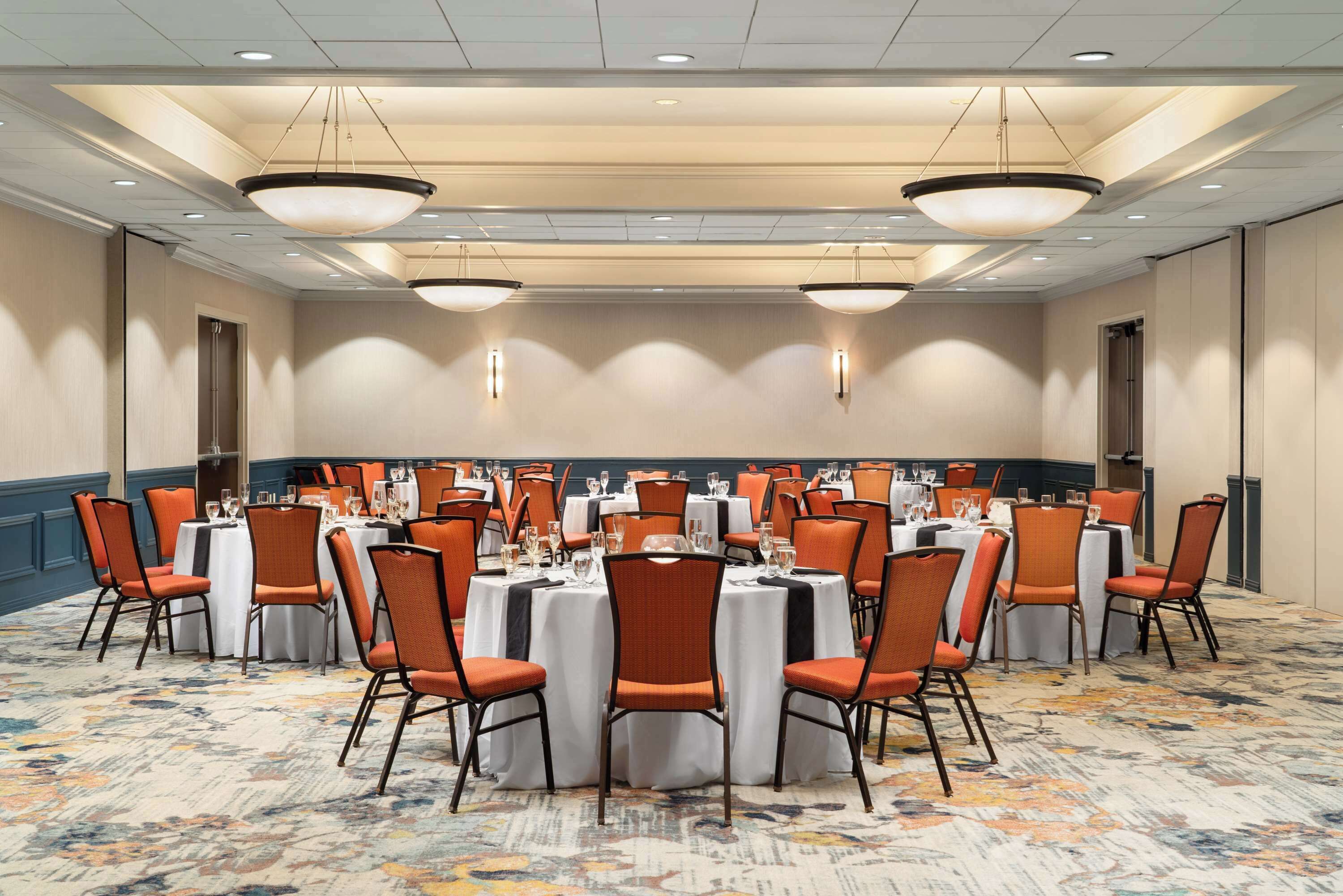 A conference room with round tables, orange chairs, and white tablecloths.