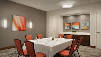 Un salón de conferencias con una mesa blanca, sillas anaranjadas y arte abstracto en la pared.