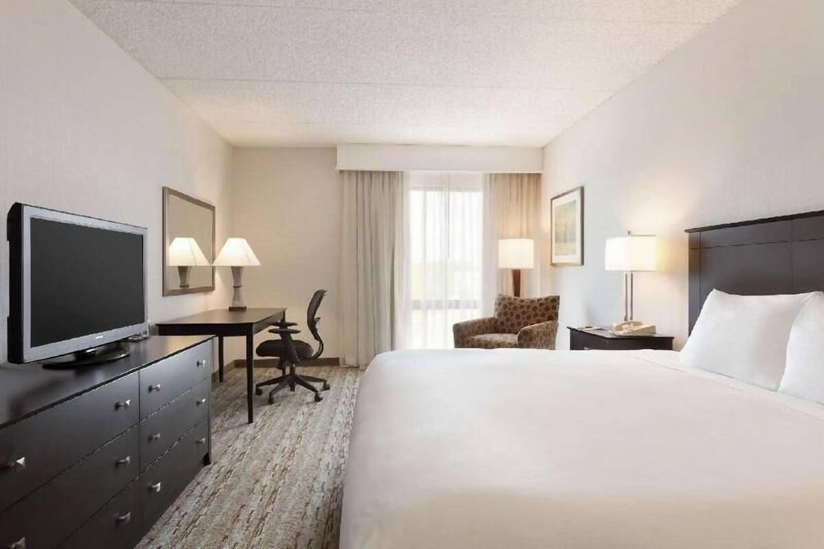 Une chambre d’hôtel comprenant un lit, un bureau, une chaise, une télévision et deux lampes.