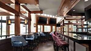 Una zona de bar con taburetes altos, una barra y un televisor montado en la pared.