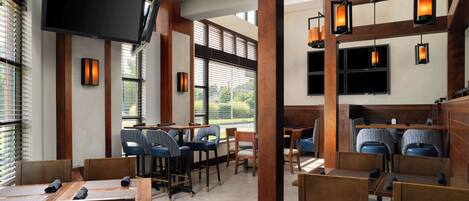 A restaurant with wooden tables and chairs, a flat-screen TV, and pendant lighting.