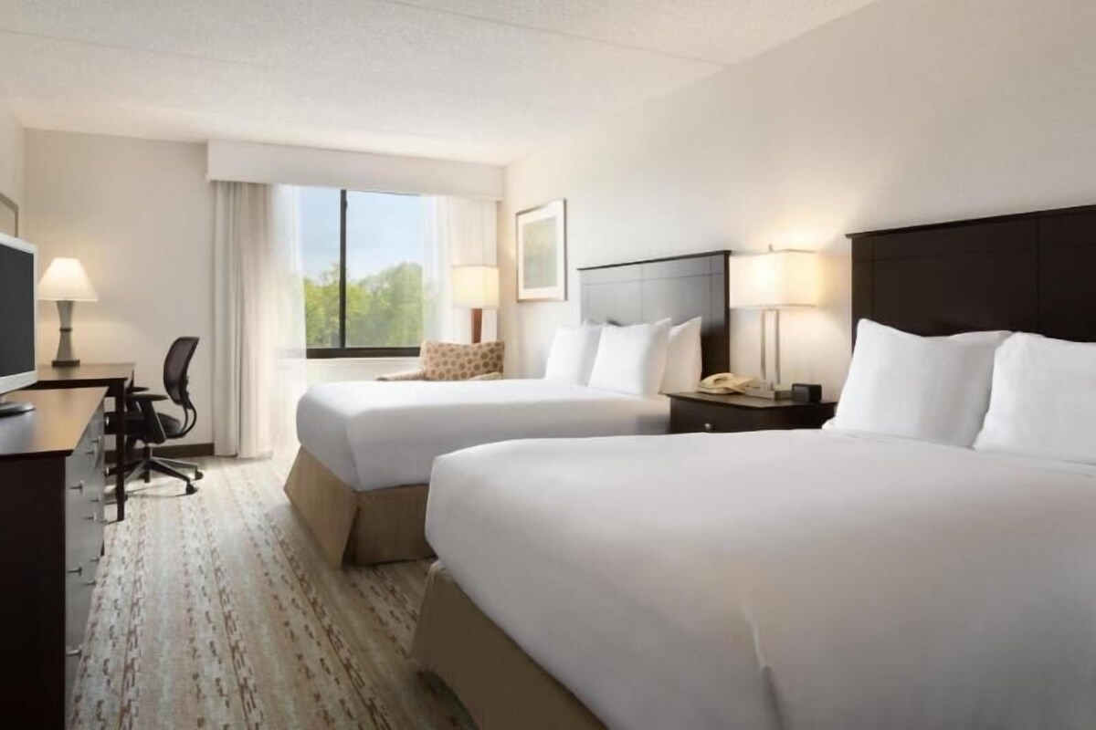 Une chambre d’hôtel avec deux lits, un bureau avec une chaise, une télévision et une fenêtre avec des rideaux.