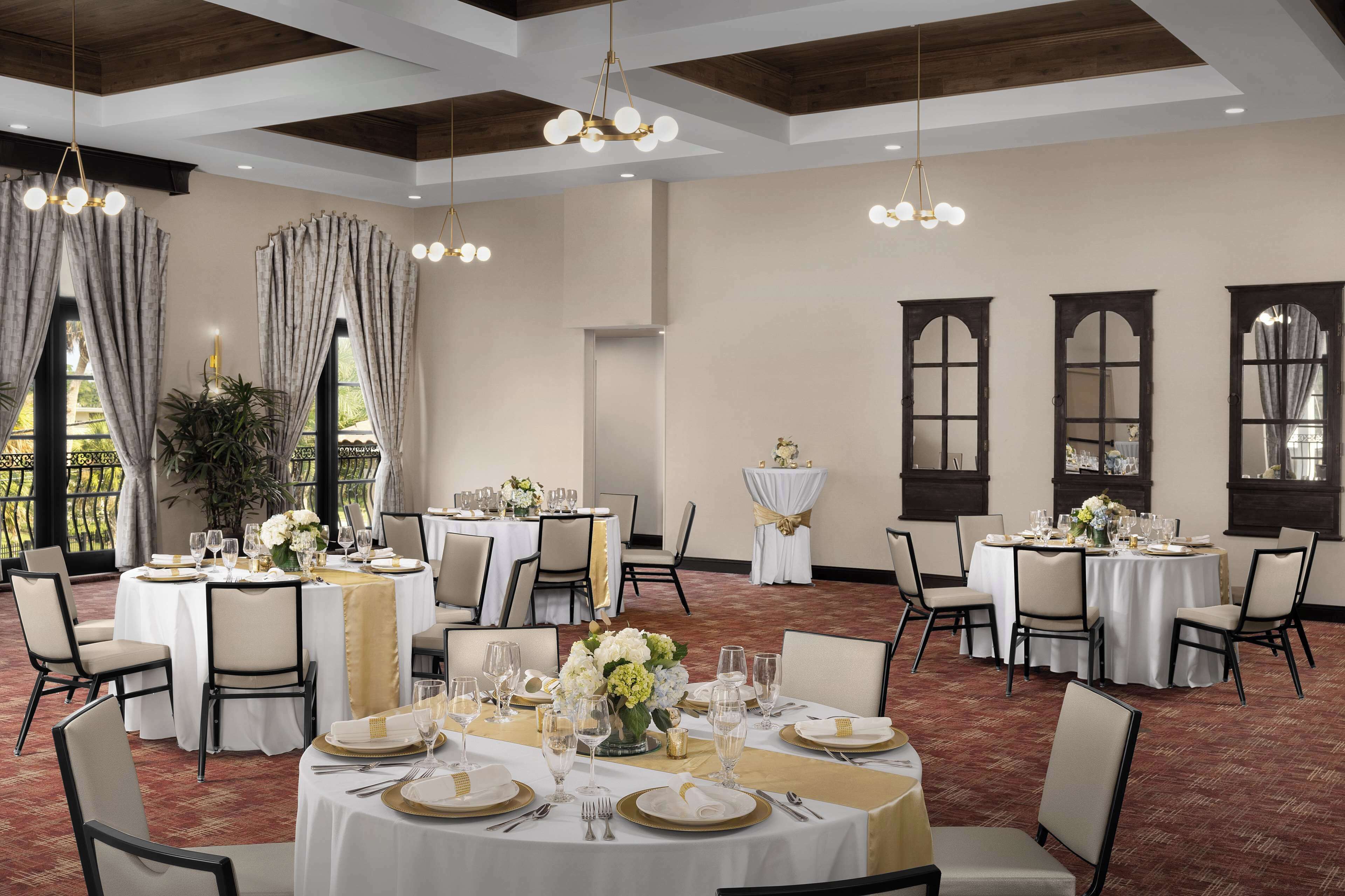 A banquet hall with round tables set for dining, featuring gold accents and white tablecloths.