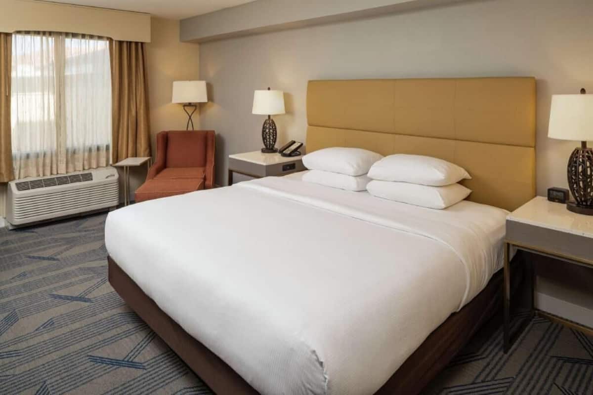 A hotel room with a large bed, two bedside tables, a chair, a desk, and a window with curtains.