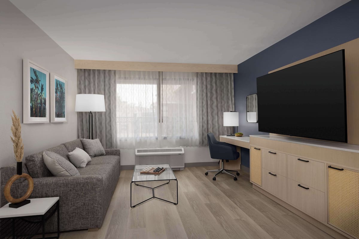 A modern living room with a grey sofa, a coffee table, a TV, and a desk with a chair.