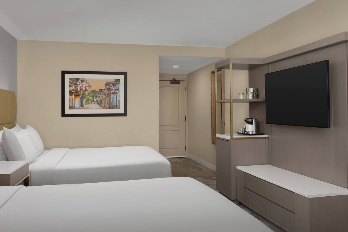 A hotel room with two beds, a flat-screen TV, a coffee machine, and a framed picture on the wall.