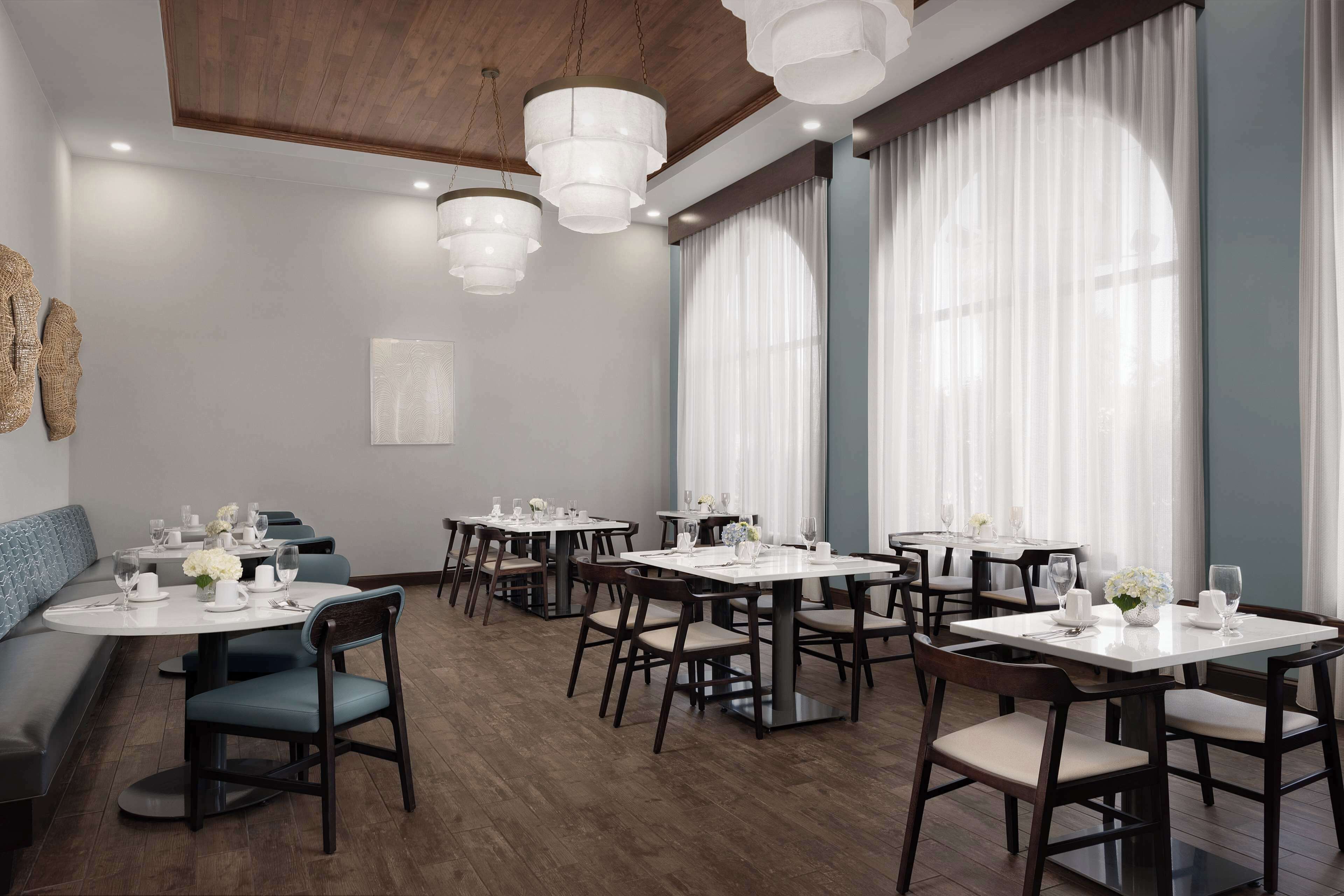 A modern dining area with round tables, dark wooden chairs, and white table settings.