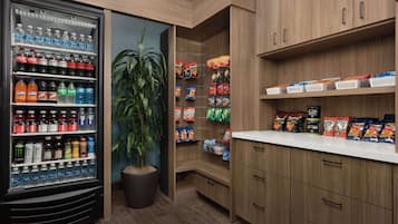 Cocina bien organizada con un refrigerador de bebidas repleto de diversas opciones, una planta en maceta y estantes con aperitivos y condimentos.