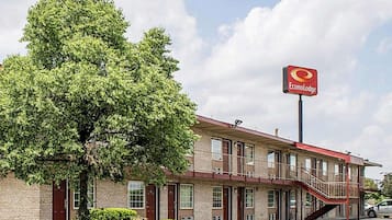 A two-story motel with a red awning, a parking lot, and a large tree in front.