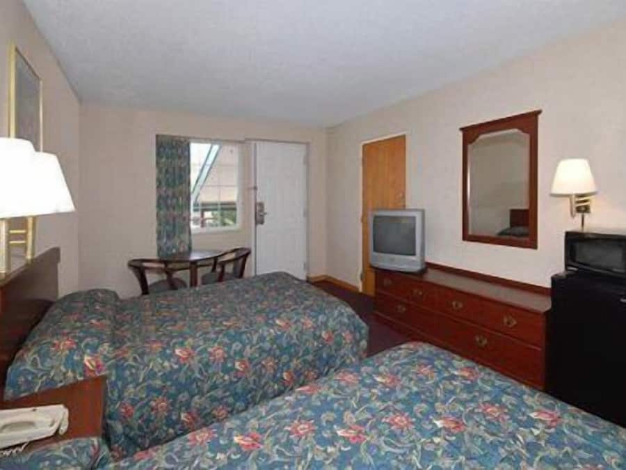 A hotel room with two beds, a desk, a television, a dresser, and a mirror.