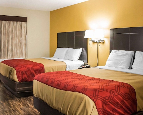 A hotel room with two beds, each with a red and beige bedspread, a nightstand with a lamp, and a window with curtains. - Econo Lodge Columbus West (Columbus)