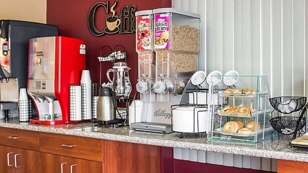 A coffee station with a red coffee machine, a Keurig coffee maker, and a display of Frosted Flakes and Raisin Bran cereals. - Econo Lodge Columbus West (Columbus)