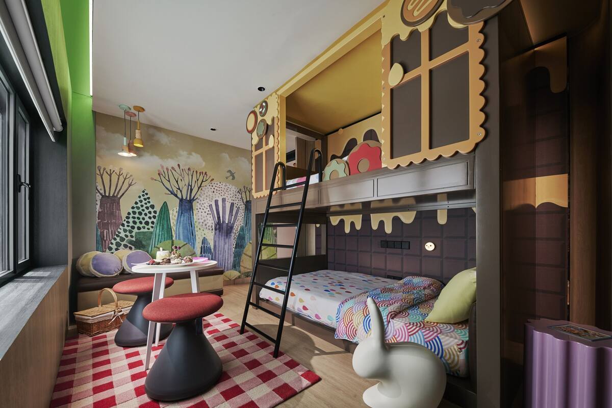 Une salle de jeux pour enfants avec un lit superposé, une échelle, une petite table et une fresque colorée sur le mur.
