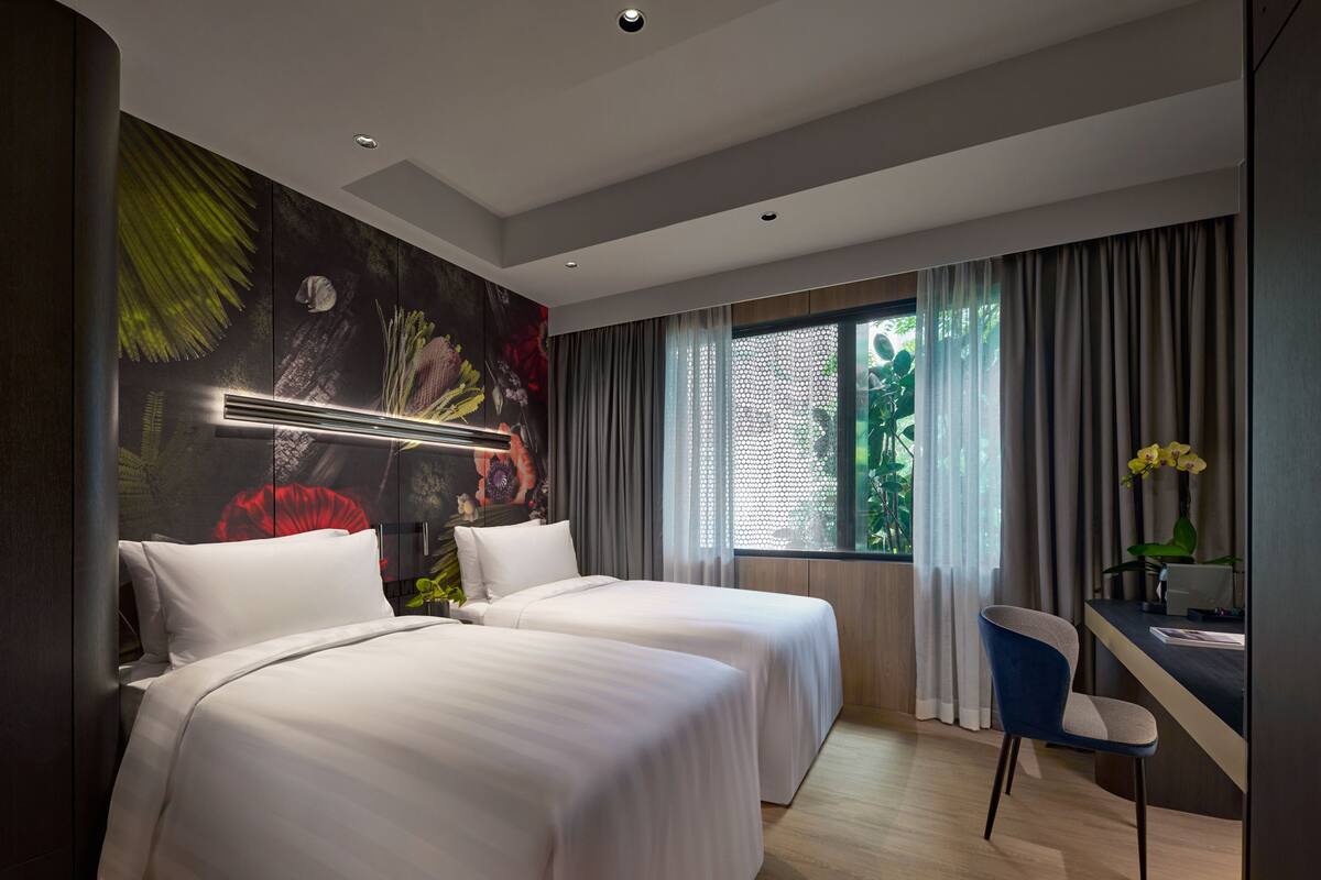 Une chambre d’hôtel moderne avec deux lits, un bureau et une grande fenêtre avec des rideaux.