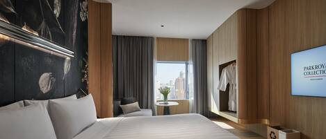 A modern hotel room with a large bed, a view of the city, a small table with a vase, and a TV displaying 'PARKROYAL COLLECTION KUALA LUMPUR'.
