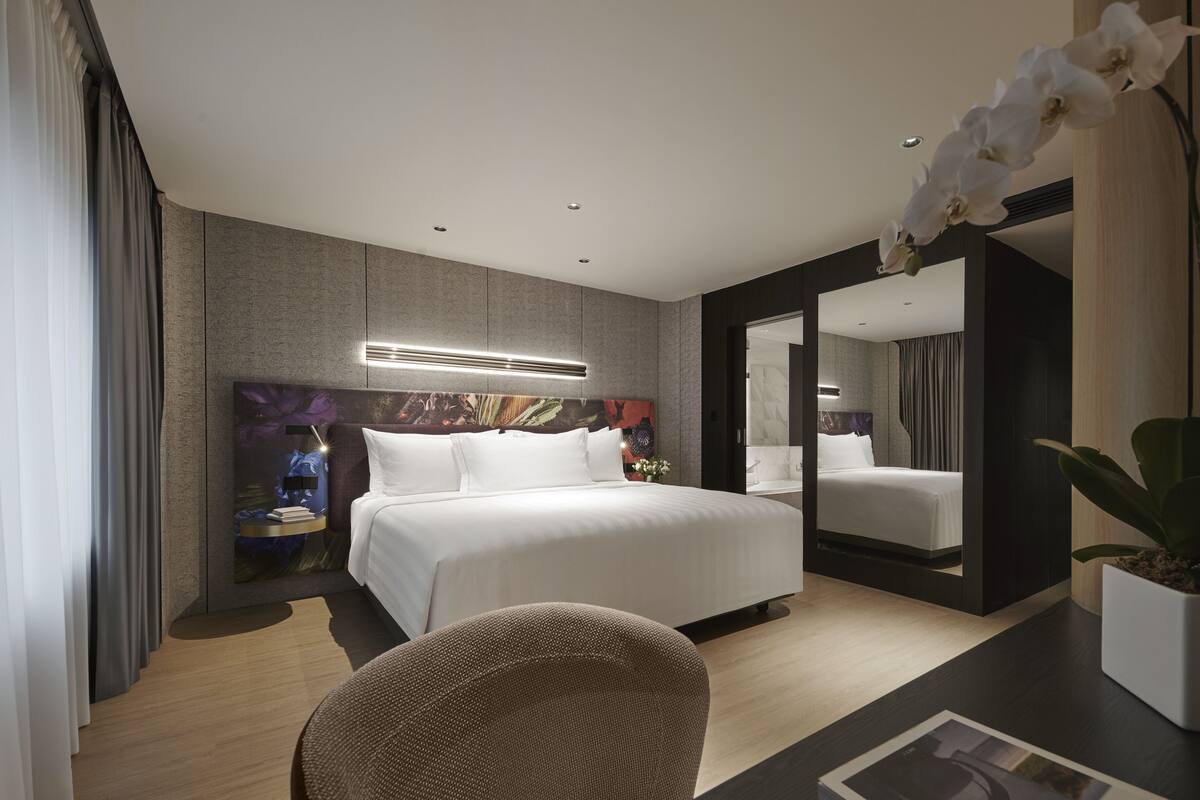 Une chambre d’hôtel moderne avec un grand lit, une table de chevet avec une lampe, un téléviseur fixé au mur et une plante en pot.