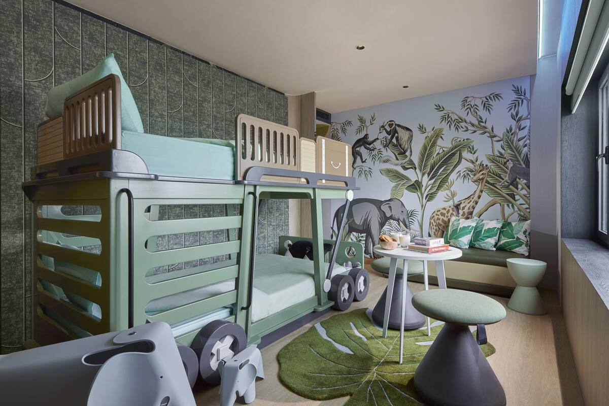 Un espace de jeux pour enfants avec un parc en plastique vert, une petite table et une fresque représentant des animaux de la jungle sur le mur.