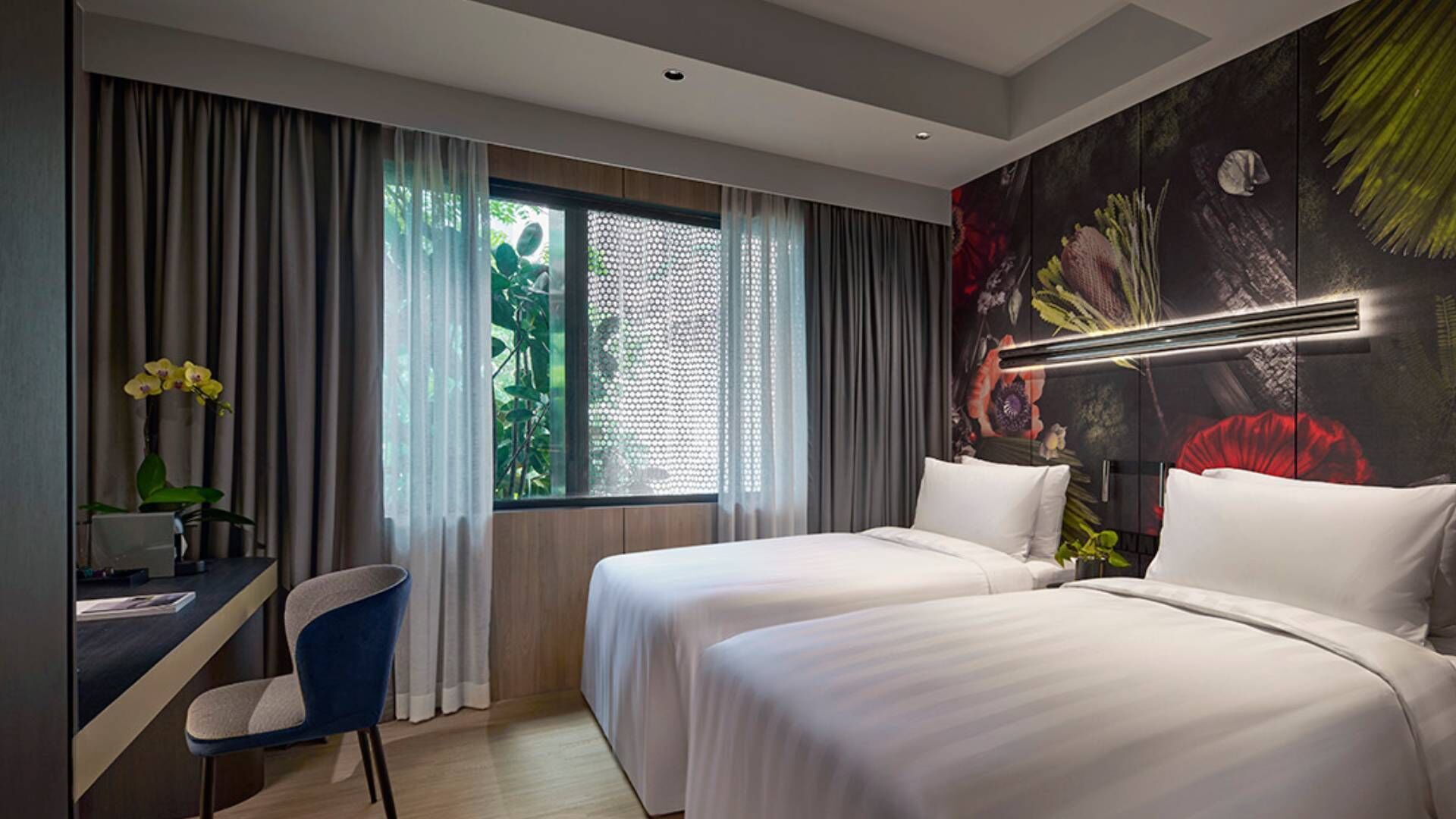 Una habitación de hotel con dos camas, un escritorio, una silla y un ventanal con cortinas.
