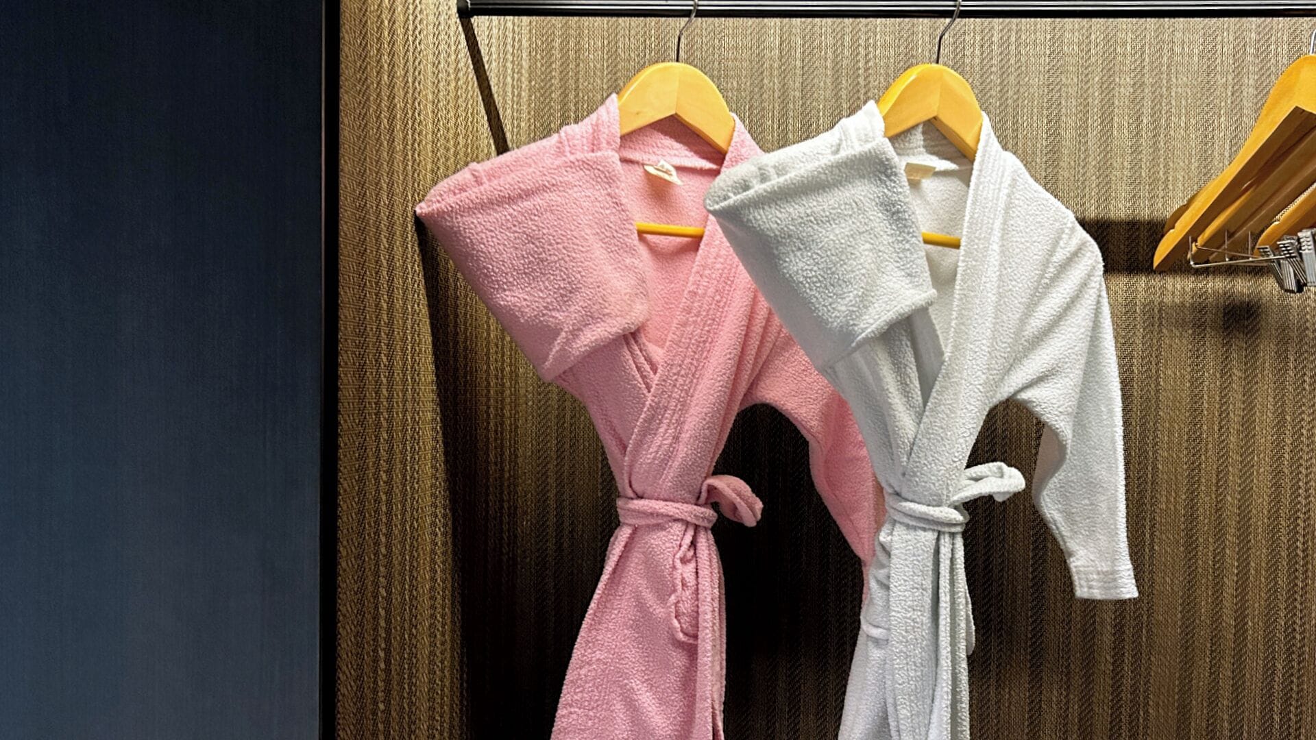 Two robes hanging on wooden hangers against a textured wall.