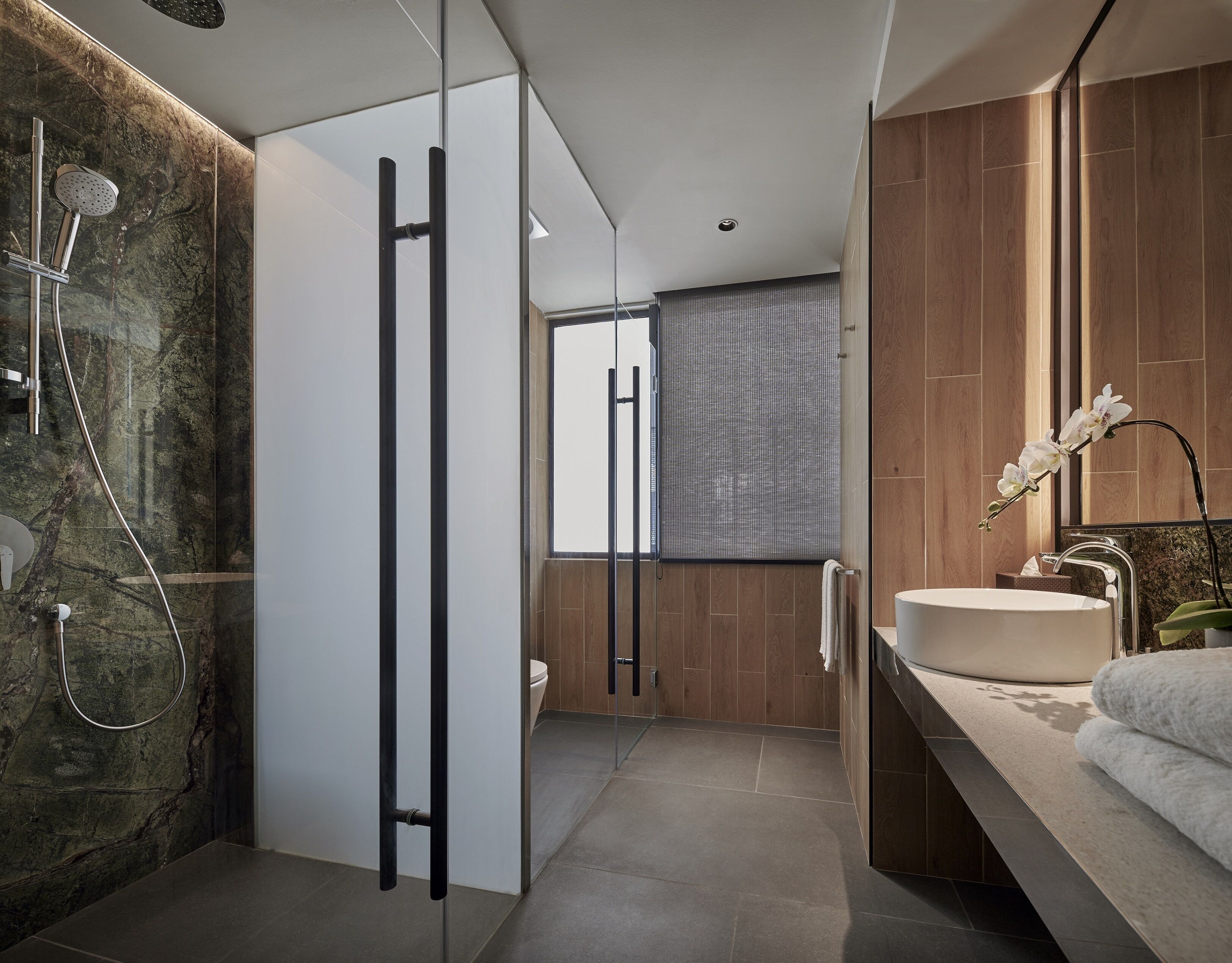 Un baño moderno con cabina de ducha de vidrio, un espejo grande y un lavabo redondo.