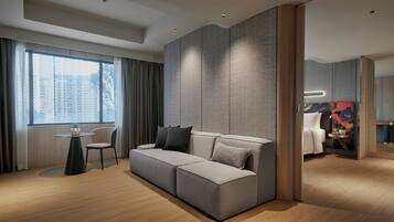 A modern hotel room with a grey sectional sofa, a small round table, and a chair.