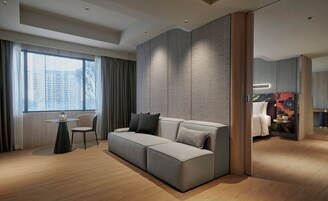 Une chambre d’hôtel moderne avec un canapé d’angle gris, une petite table ronde et une chaise.