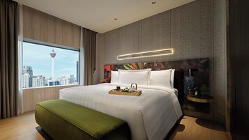 Una habitación de hotel moderna con una cama grande, vistas a un paisaje urbano y una torre de la ciudad al fondo.
