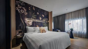 Una habitación de hotel moderna con una cama grande, una mesita de noche, una pequeña mesa con una planta y vistas a la ciudad a través de la ventana.