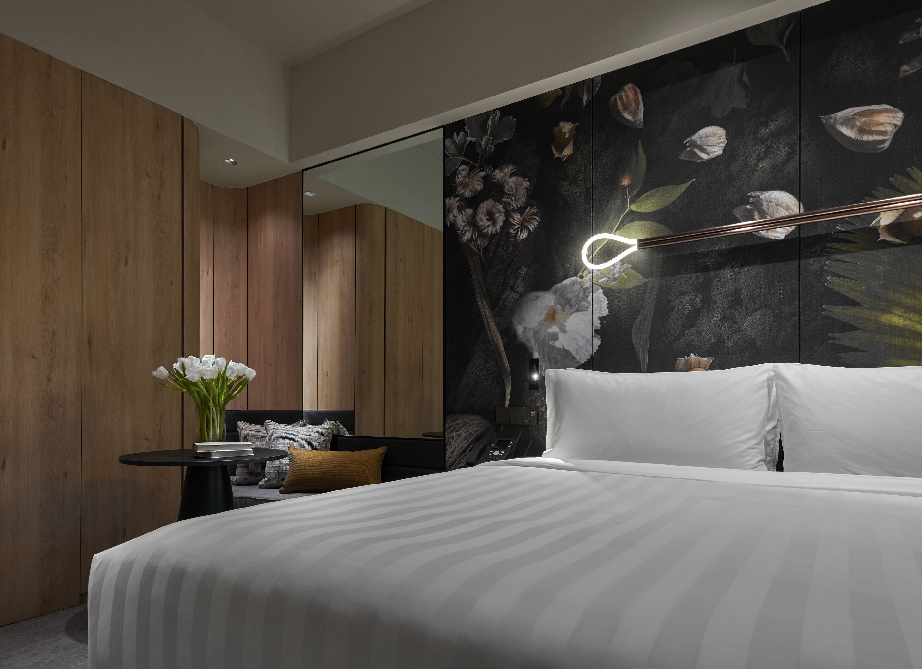 Un dormitorio moderno con una cama grande, una mesita de noche con un florero y un espejo en la pared.