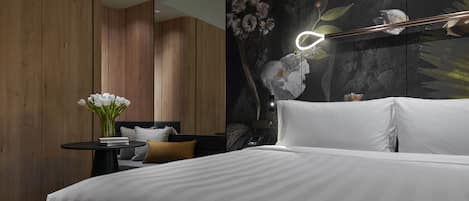 A modern bedroom with a large bed, a bedside table with a vase of flowers, and a wall-mounted mirror.