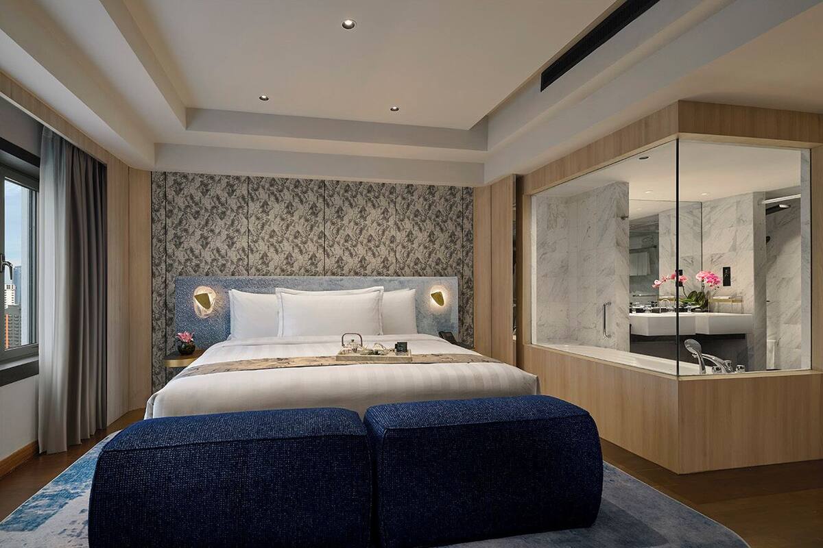 Une chambre d’hôtel moderne dotée d’un grand lit, d’un coin salon, d’un grand miroir et offrant une vue sur la salle de bain.