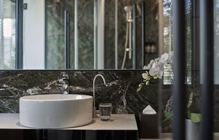 Une salle de bain avec un lavabo blanc, un verre d’eau et un arrangement floral.