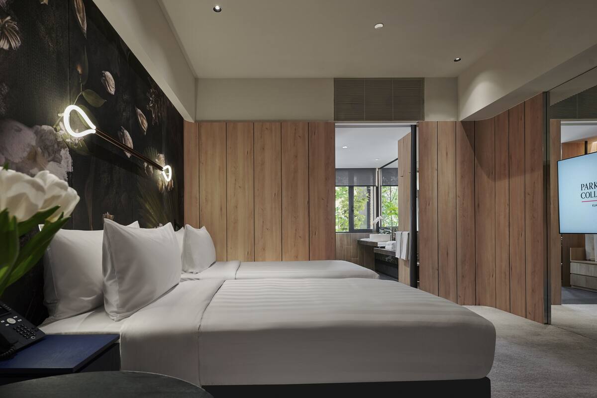 Une chambre d’hôtel moderne avec un grand lit, des murs recouverts de panneaux de bois, un luminaire fixé au mur et une vue sur l’extérieur par une fenêtre.