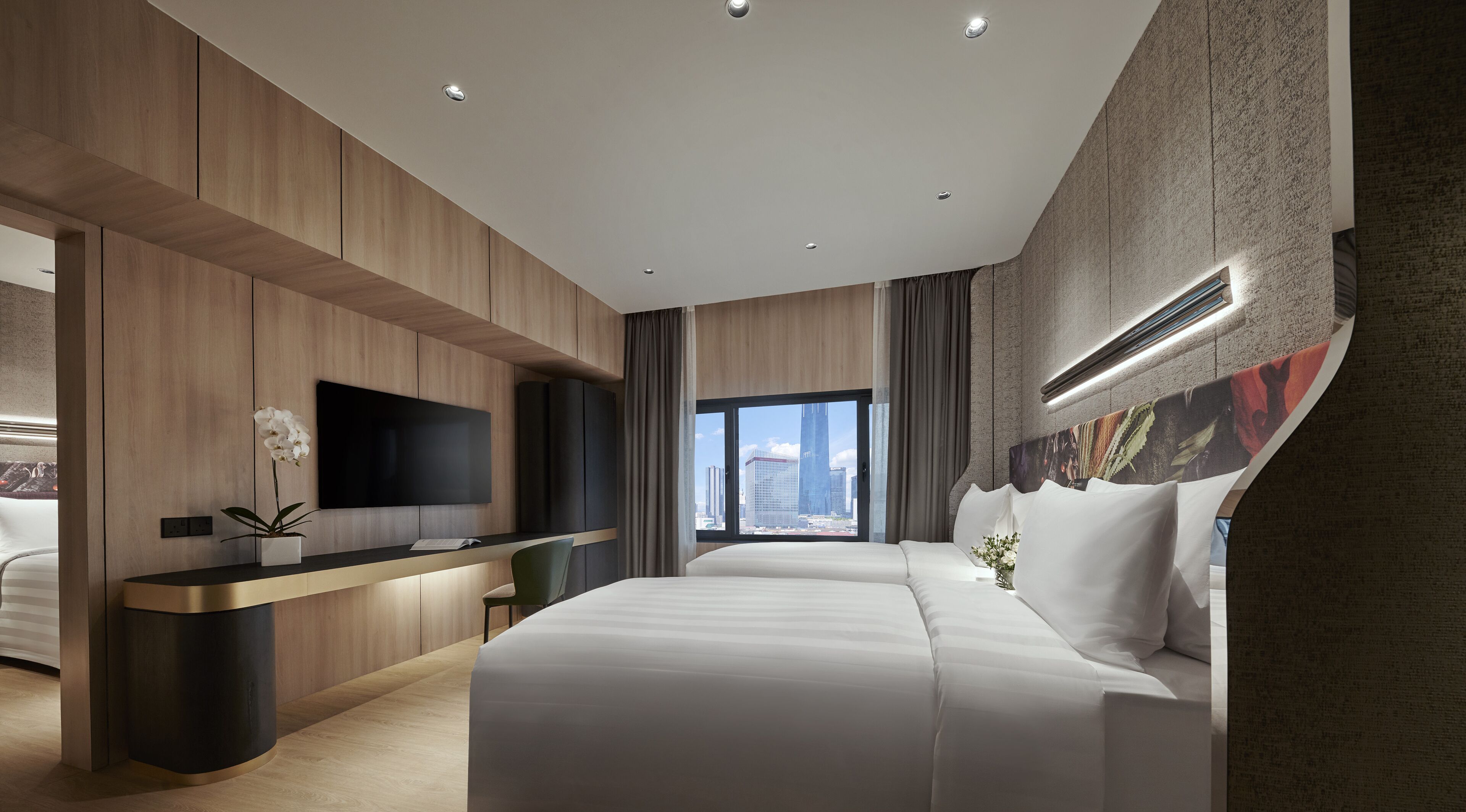 A modern hotel room with a large bed, a desk with a flat-screen TV, a view of the cityscape, and a large window with curtains.