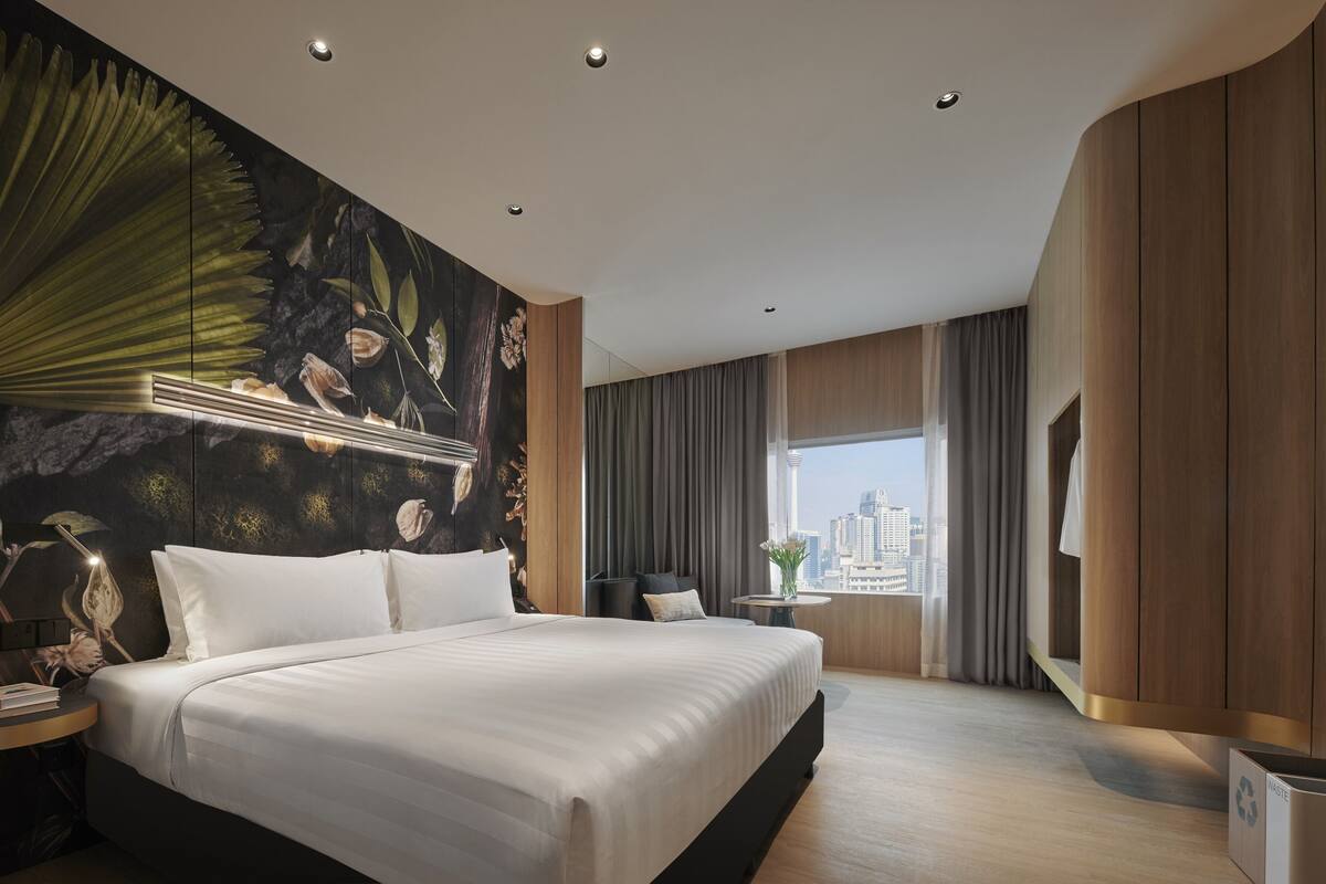 Une chambre d’hôtel moderne avec un grand lit, une vue sur la ville et une fresque murale aux motifs tropicaux.