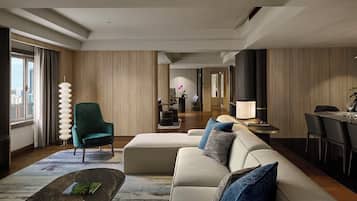 A modern hotel room with a sofa, armchair, dining table, and a view of the city through large windows.