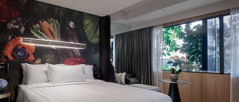 Una habitación de hotel moderna con una cama grande, un mural en la pared, una ventana con vistas a zonas verdes y una pequeña mesa con una planta.