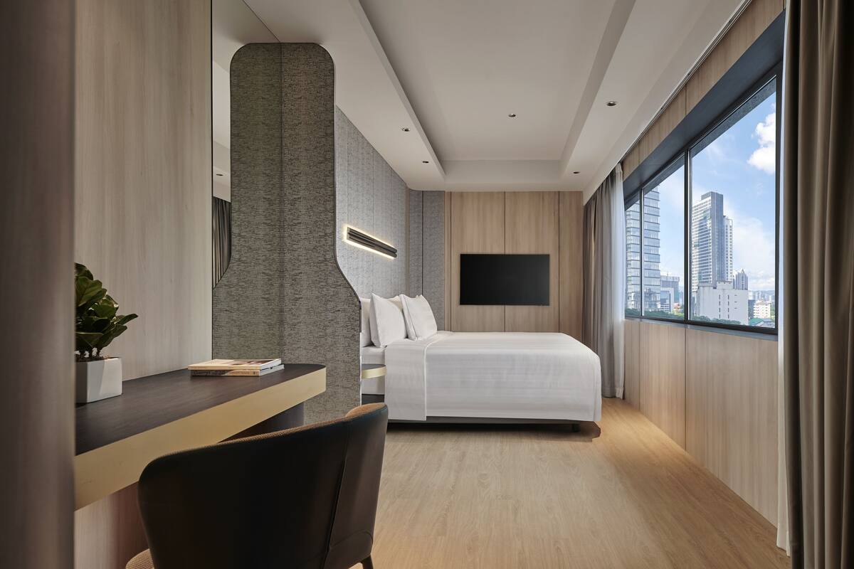 Une chambre d’hôtel moderne équipée d’un lit, d’un bureau, d’une chaise, d’une télévision et d’une grande fenêtre donnant sur la ville.