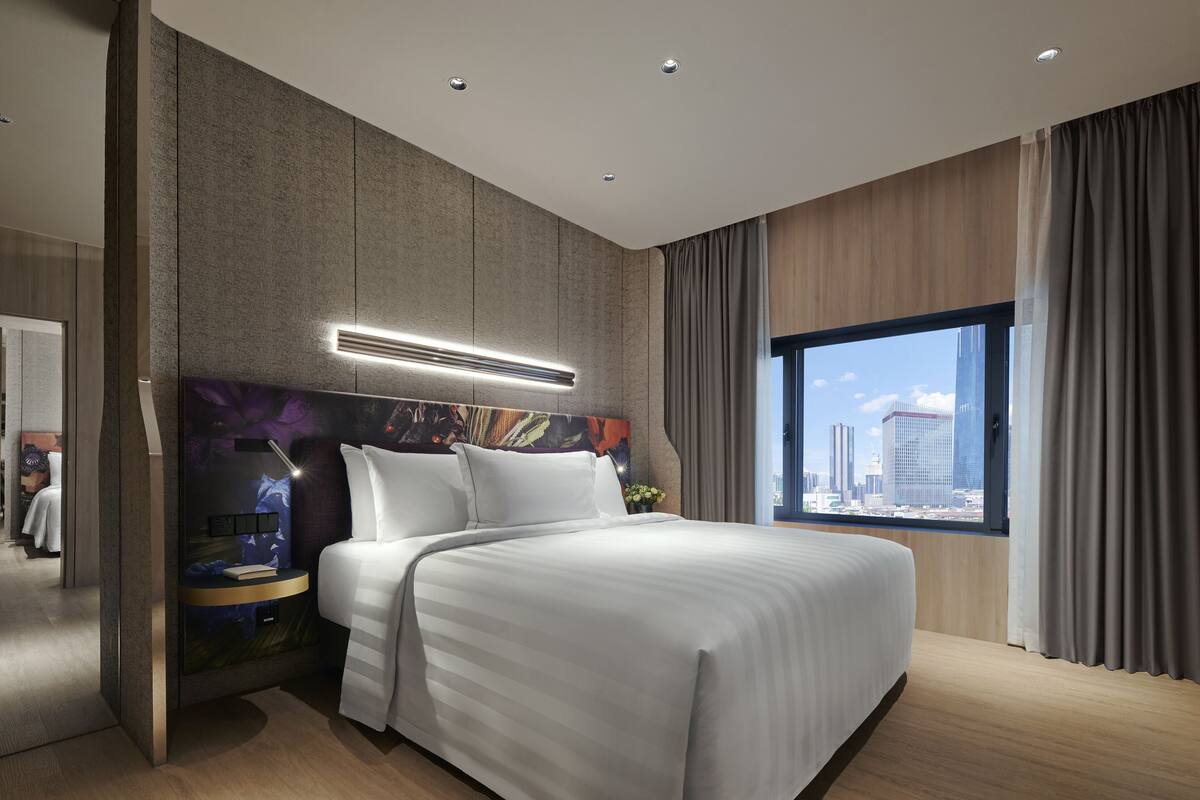 Une chambre d’hôtel moderne dotée d’un grand lit, d’une télévision à écran plat, d’une table de chevet et offrant une vue sur le panorama urbain.