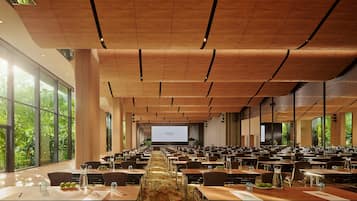 A spacious conference room with long tables, a large screen at the front, and large windows offering a view of greenery.